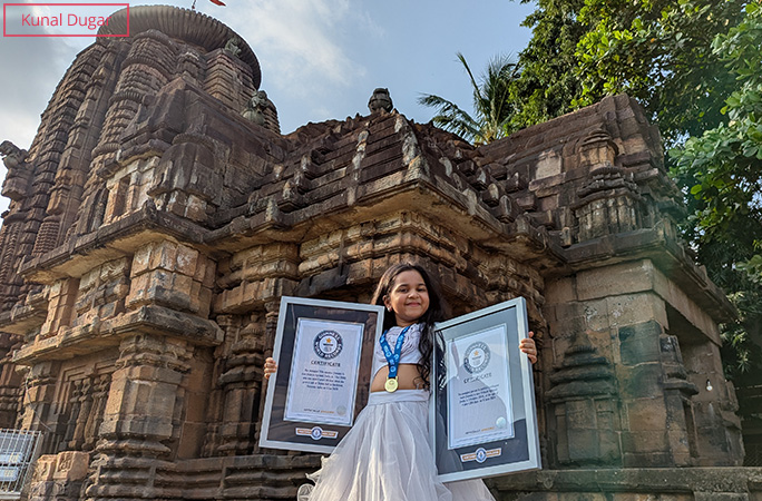 Anvi holding her two framed GWR certificates in front of a temple