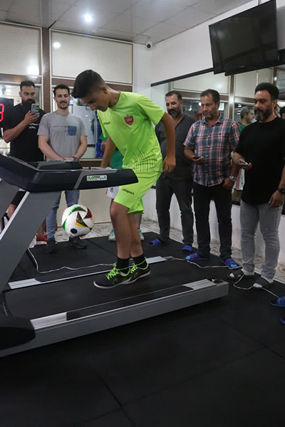 Meraj on a treadmill juggling a football with his feet with people watching 