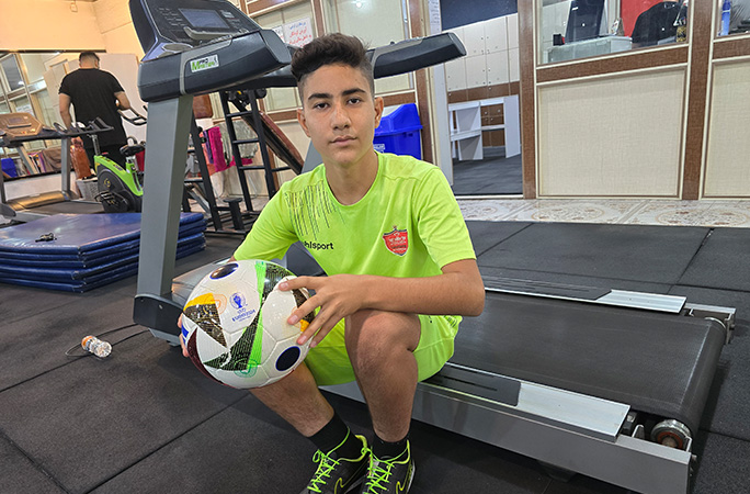 Meraj sat on the side of a treadmill holding a football