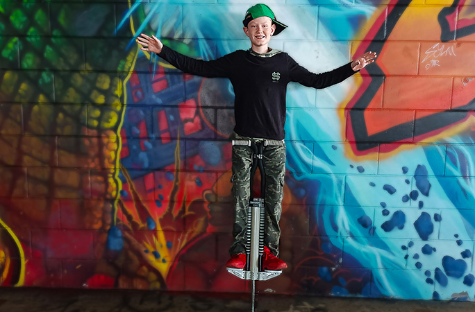 Lachlan balancing on his pogo stick without holding on with his hands in front of a graffitied wall