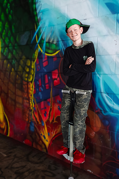 Lachlan stood on his pogo stick with his arms crossed leaning against a graffitied wall