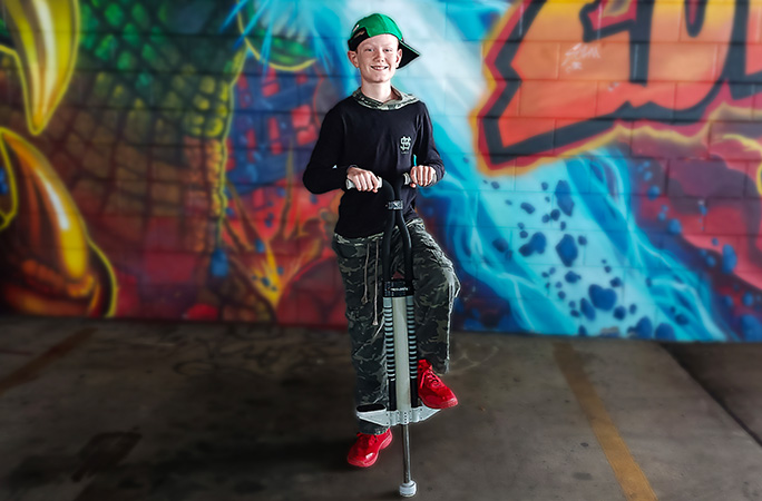 Lachlan stood with one foot on his pogo stick in front of a graffitied wall