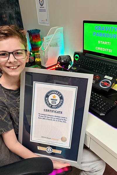 Max holding his GWR certificate with his game on the laptop screen behind him