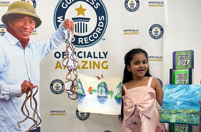 Anvi holding her painting and the painting by the man with the longest fingernails next to a cutout of him