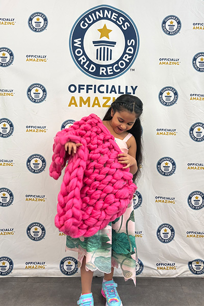 Anvi looking amazed by a pink arm knitted blanket