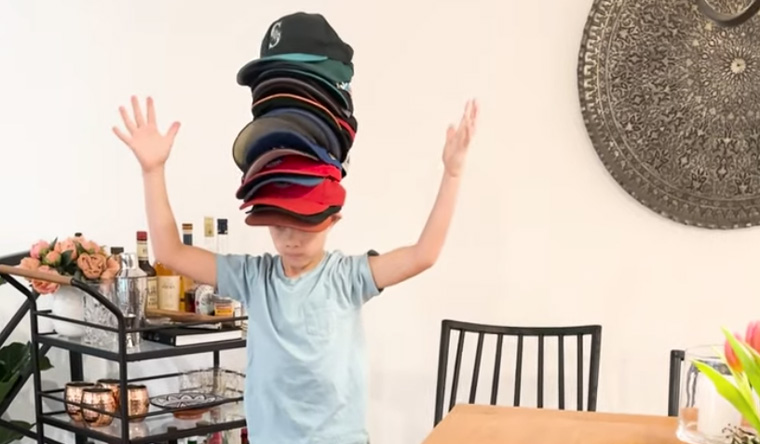 Kid with many baseball caps balanced on head 