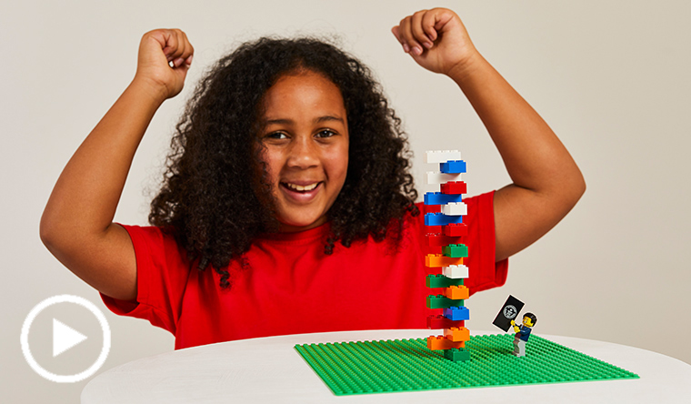 girl building lego tower with arms raised