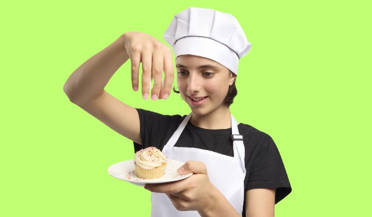 Girl with chefs hat holding a cupcake on a plate
