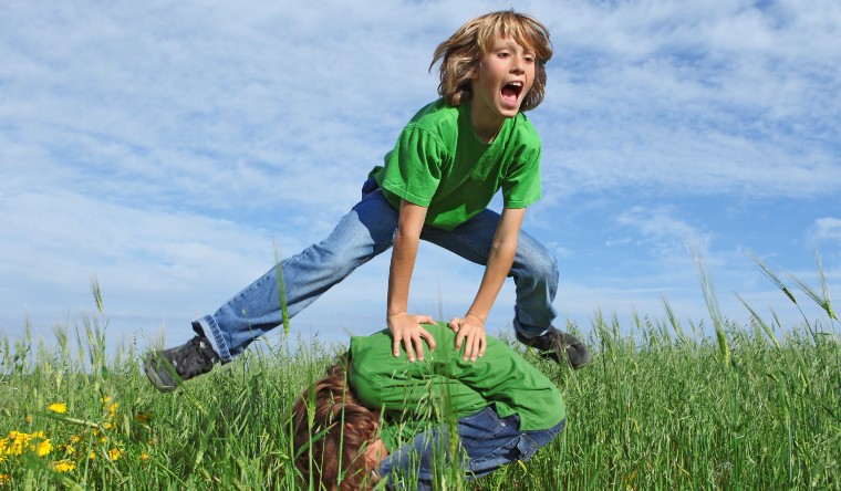 Boy leapfrogging over another boy in a field of grass