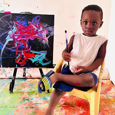 Ace Liam holding a paintbrush sat next to one of his paintings